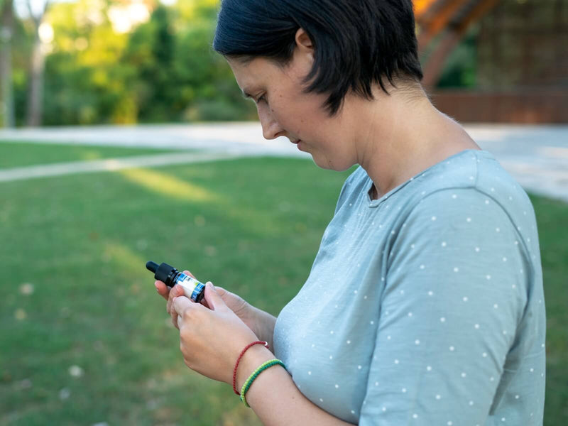 Frau betrachtet im Freien eine Flasche CBD-Öl von Formula Swiss in ihrer Hand