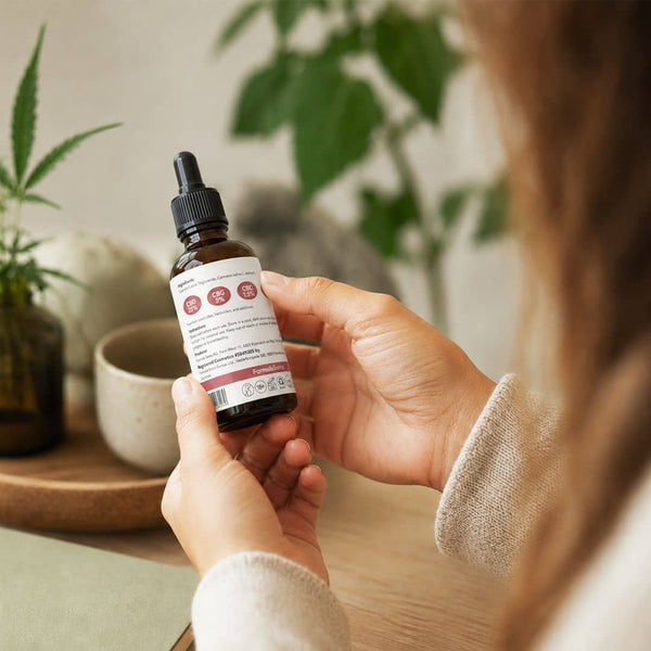 Frau, die das Etikett auf einer Formel-Schweizer Cannabinoid-Ölflasche in einer hellen Innenumgebung überprüft.