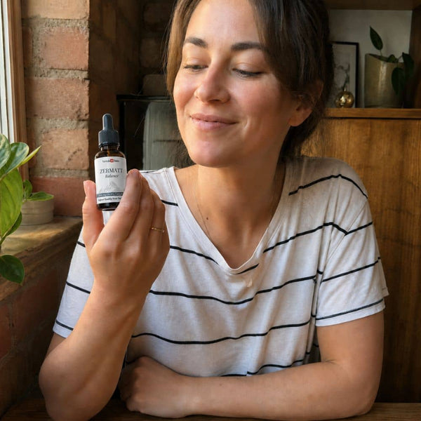 Frau, die eine Flasche Zermatter CBD Öl in einer gemütlichen Innenumgebung hält.